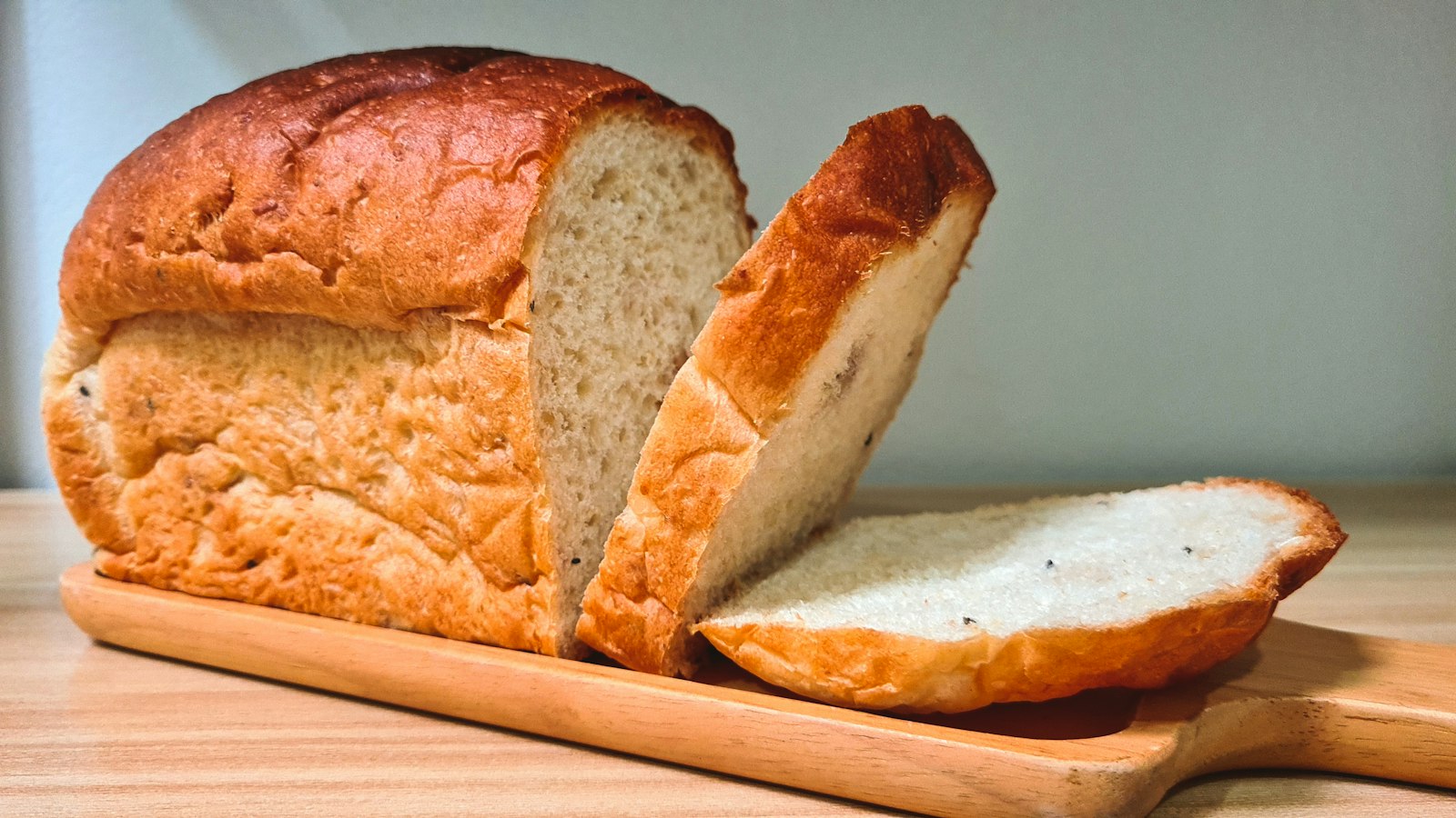 Angeschnittenes Brot mit zwei Scheiben auf einem hellen Holzbrett