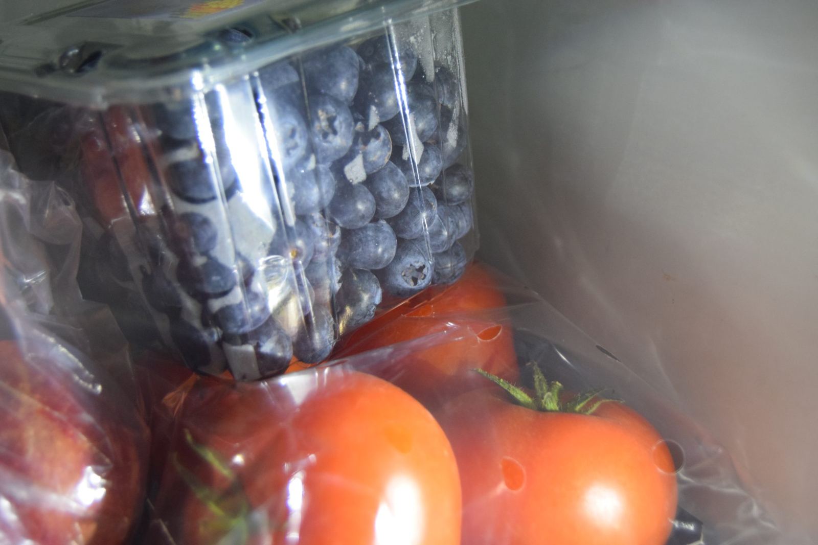 Blick in einen Kühlschrank mit Heidelbeeren in einer Box über frischen Tomaten