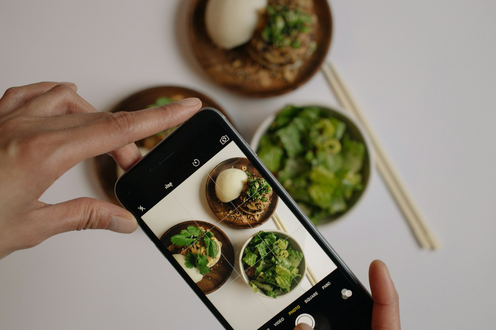 Hände fotografieren mit dem Smartphone zwei Schalen mit Ei, Kräutern und grünem Salat von oben