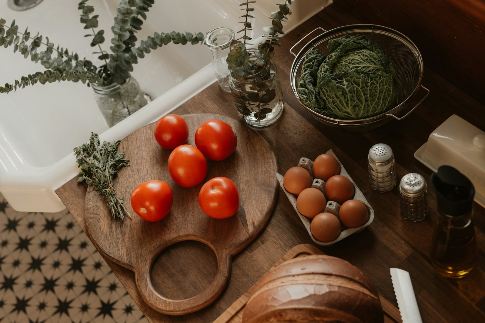 Tomaten auf einem Holzbrett, daneben Eier, Kohl, Brot und Gewürze auf einer Küchenarbeitsplatte