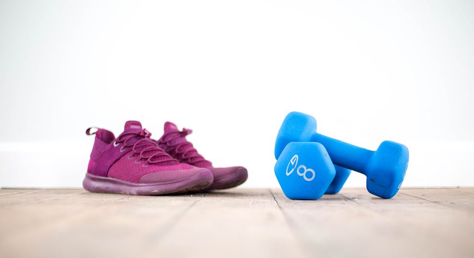 Pinke Sportschuhe und zwei blaue Kurzhanteln auf einem Holzboden