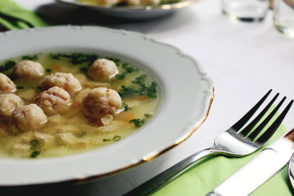 Teller mit klarer Suppe, Klößchen und frischer Petersilie, daneben eine Gabel